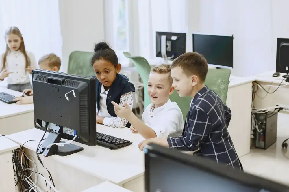 Children smiling and collaborating at a computer screen