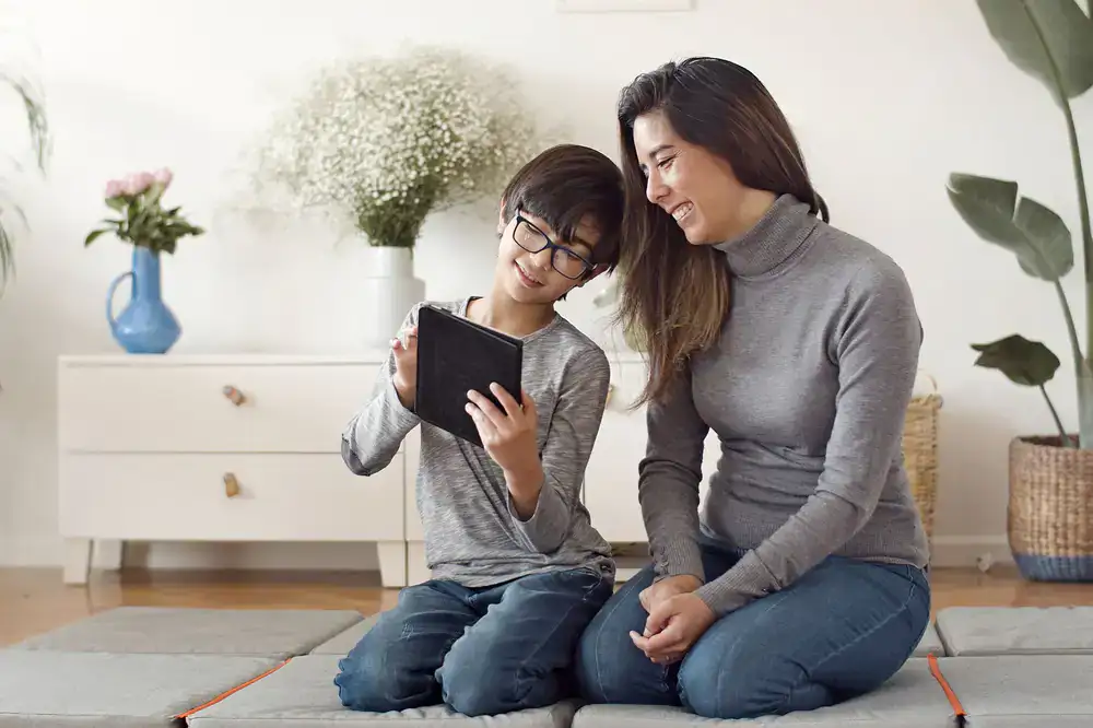 A parent smiling alongside their child who is proudly showing a tablet screen